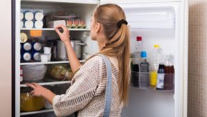 A woman performs fridge maintenance.